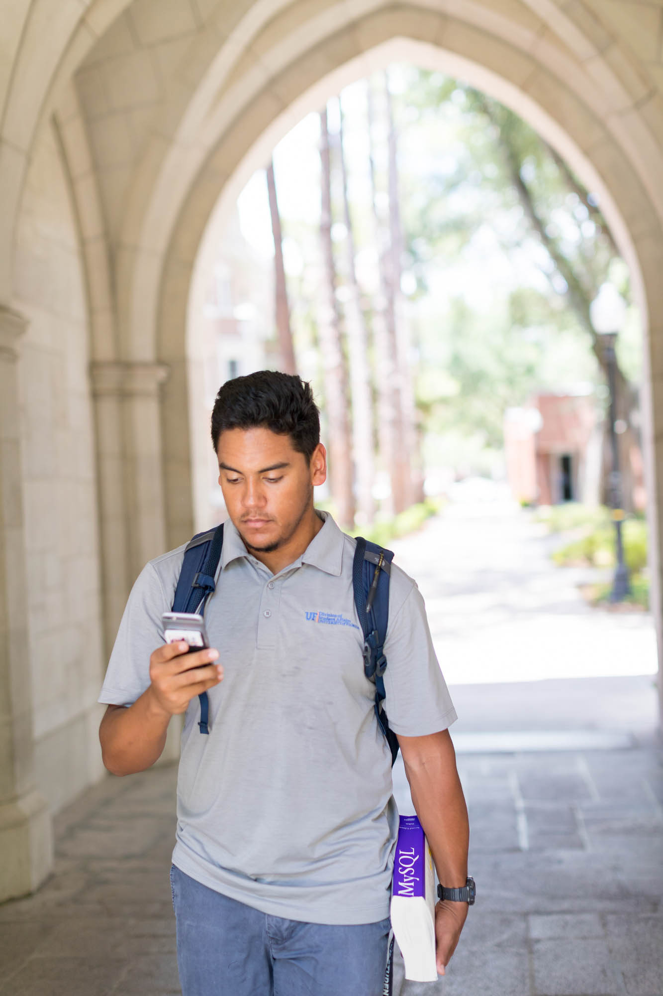 A student looks at their phone while walking through the arches of Sledd Hall. 