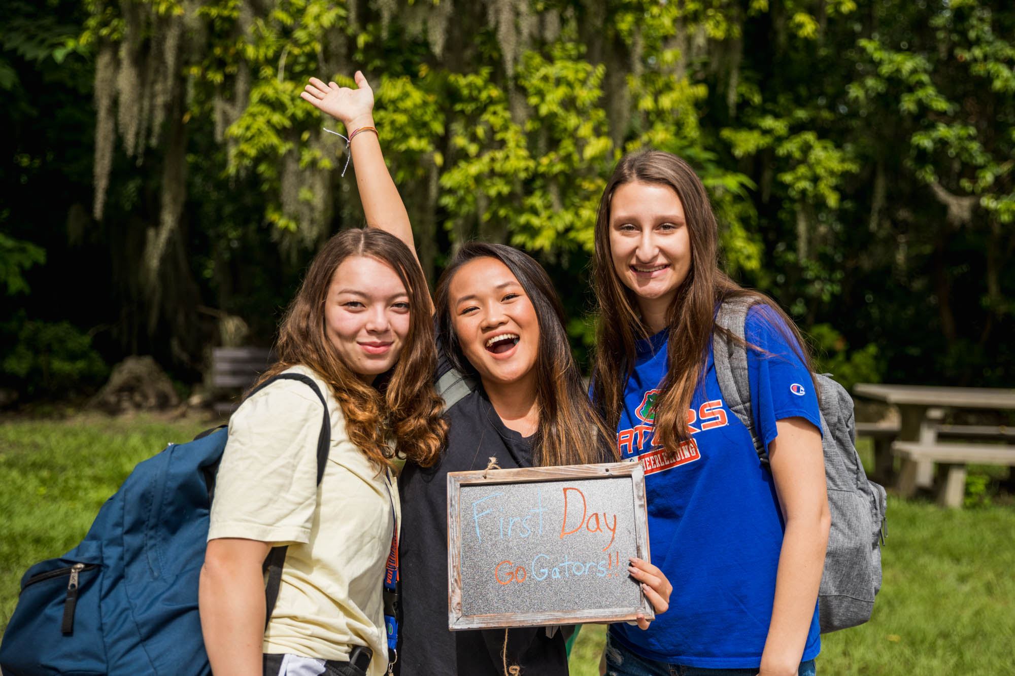 Three student smile and hold a "First Day of Class" sign.