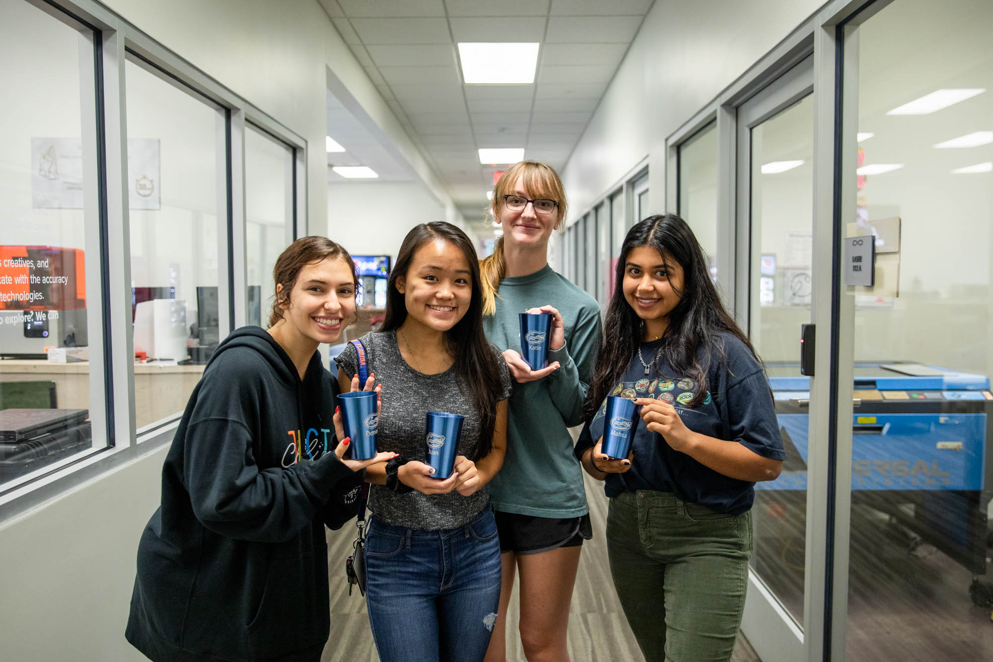4 students hold up engraved mugs made in infinity hall.