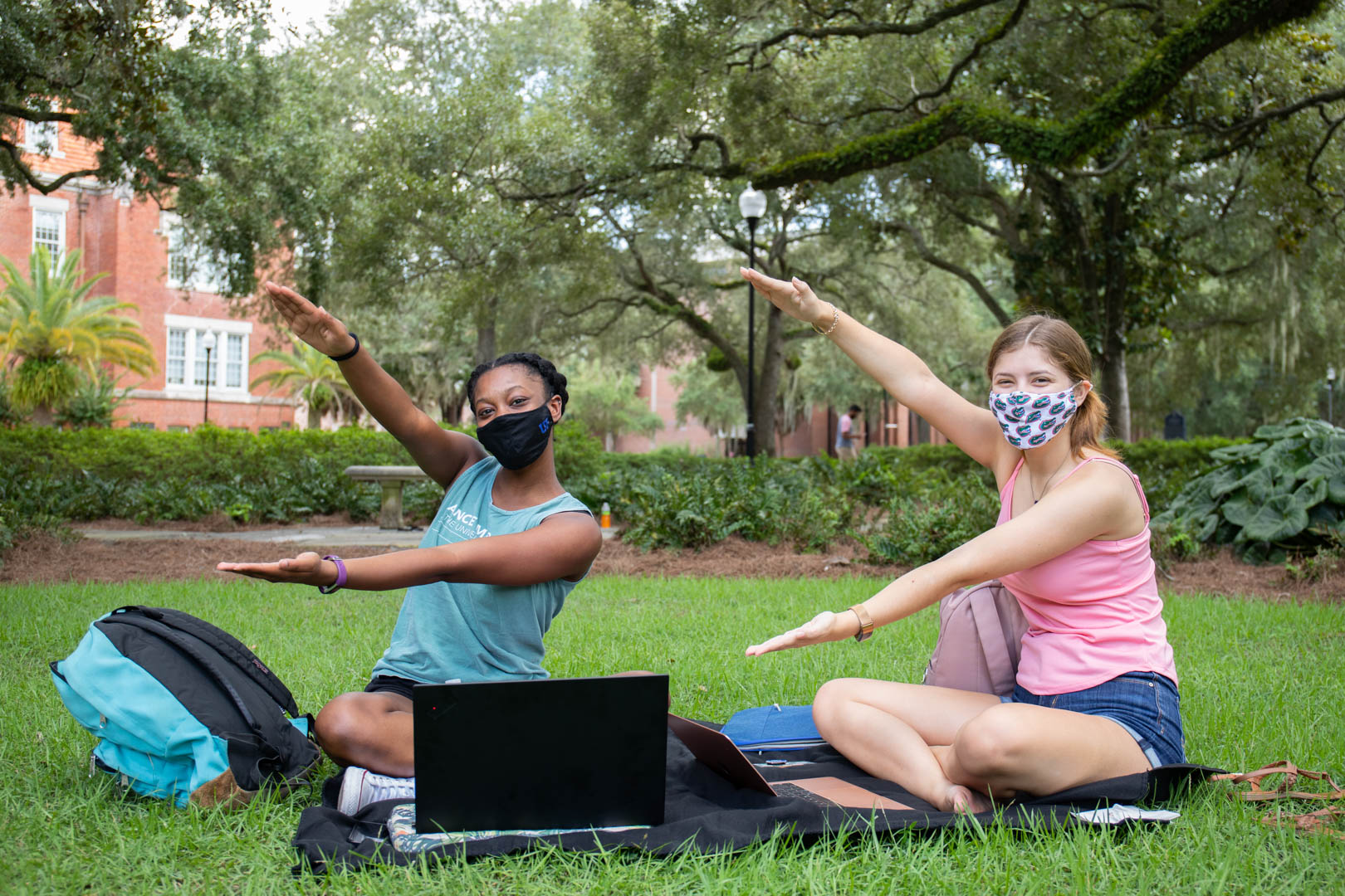 Two female students do a gator chomp while sitting on a lawn.