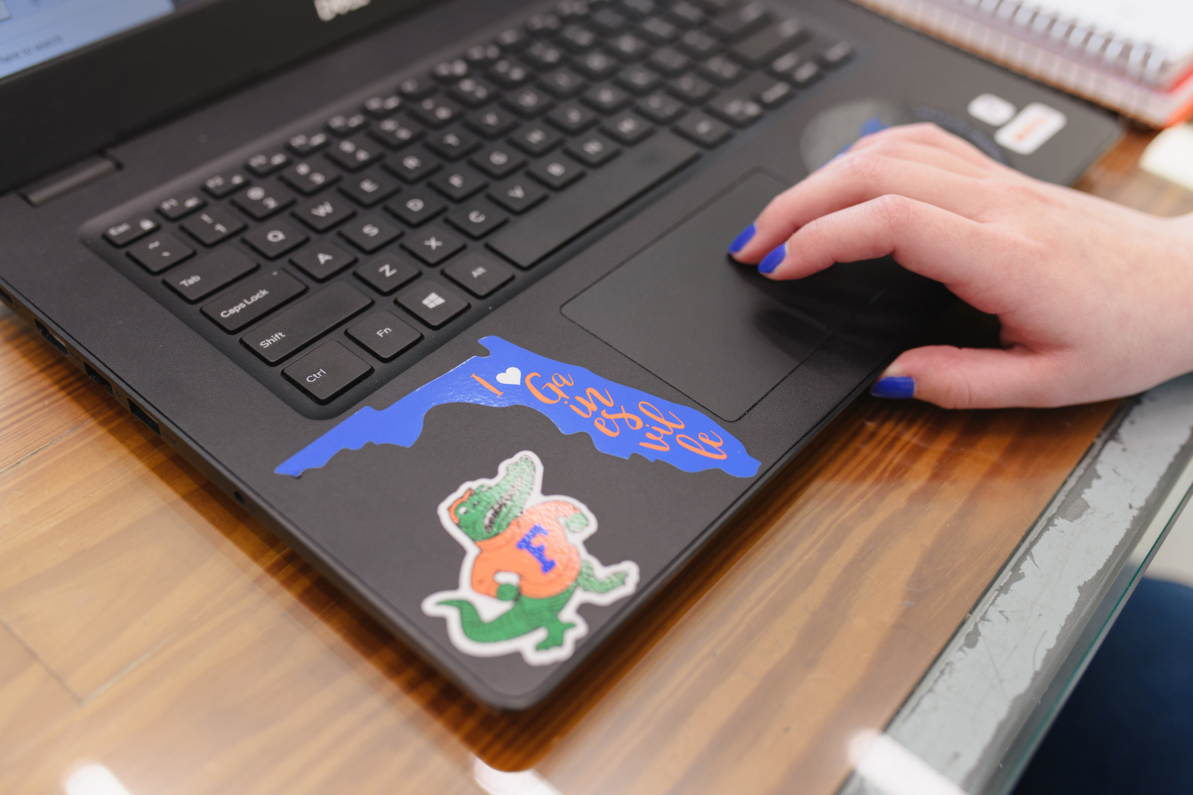 A students hand on a laptop with two gator stickers.