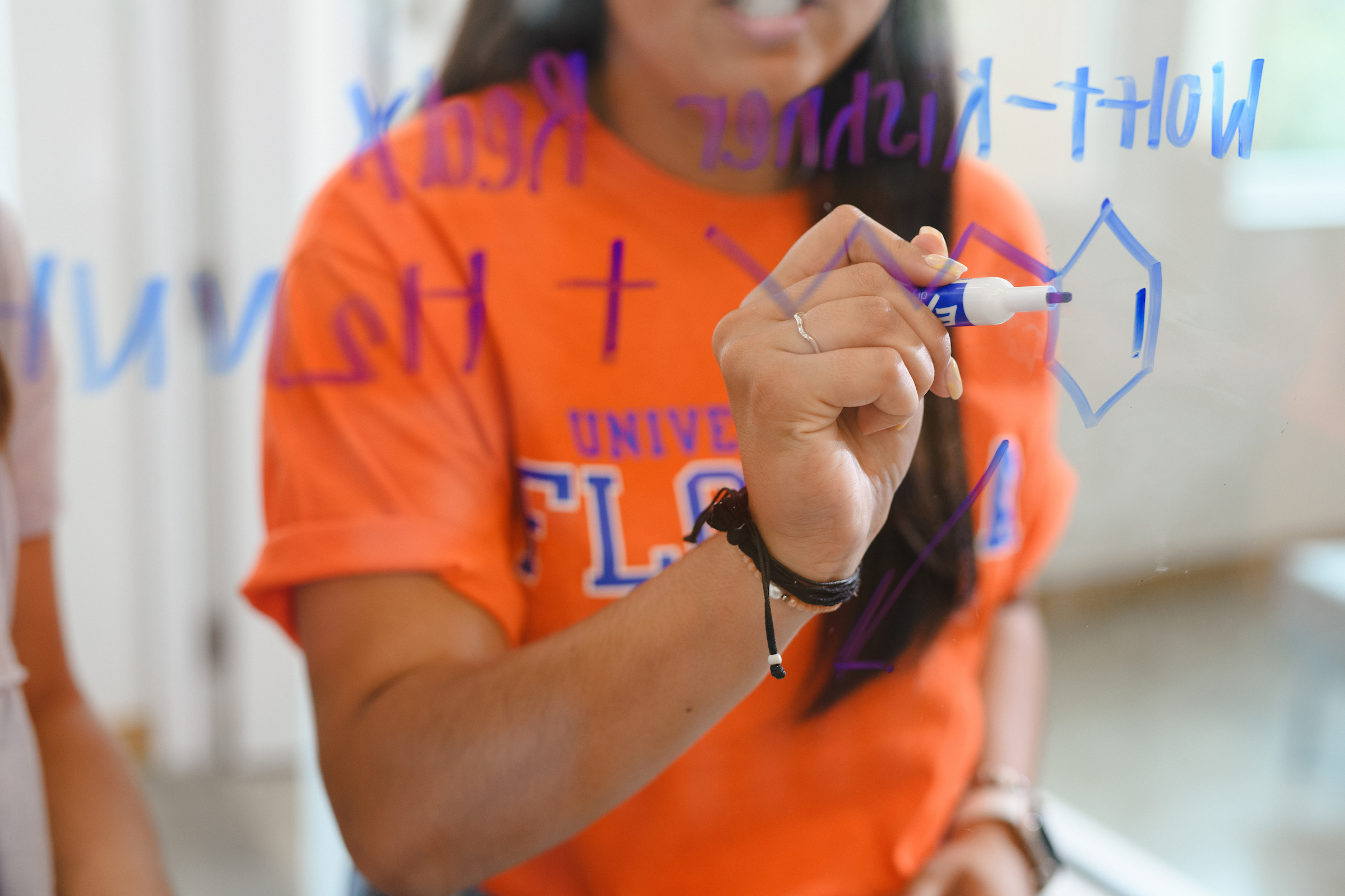 A student writes chemistry formulason glass with an expo marker.