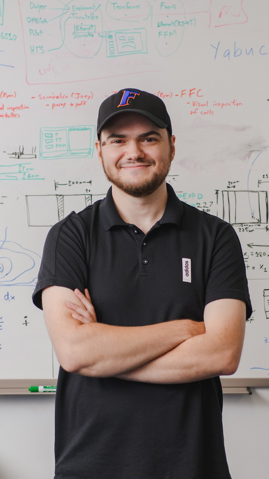 a student stands with their arams crossed in front of a white board.