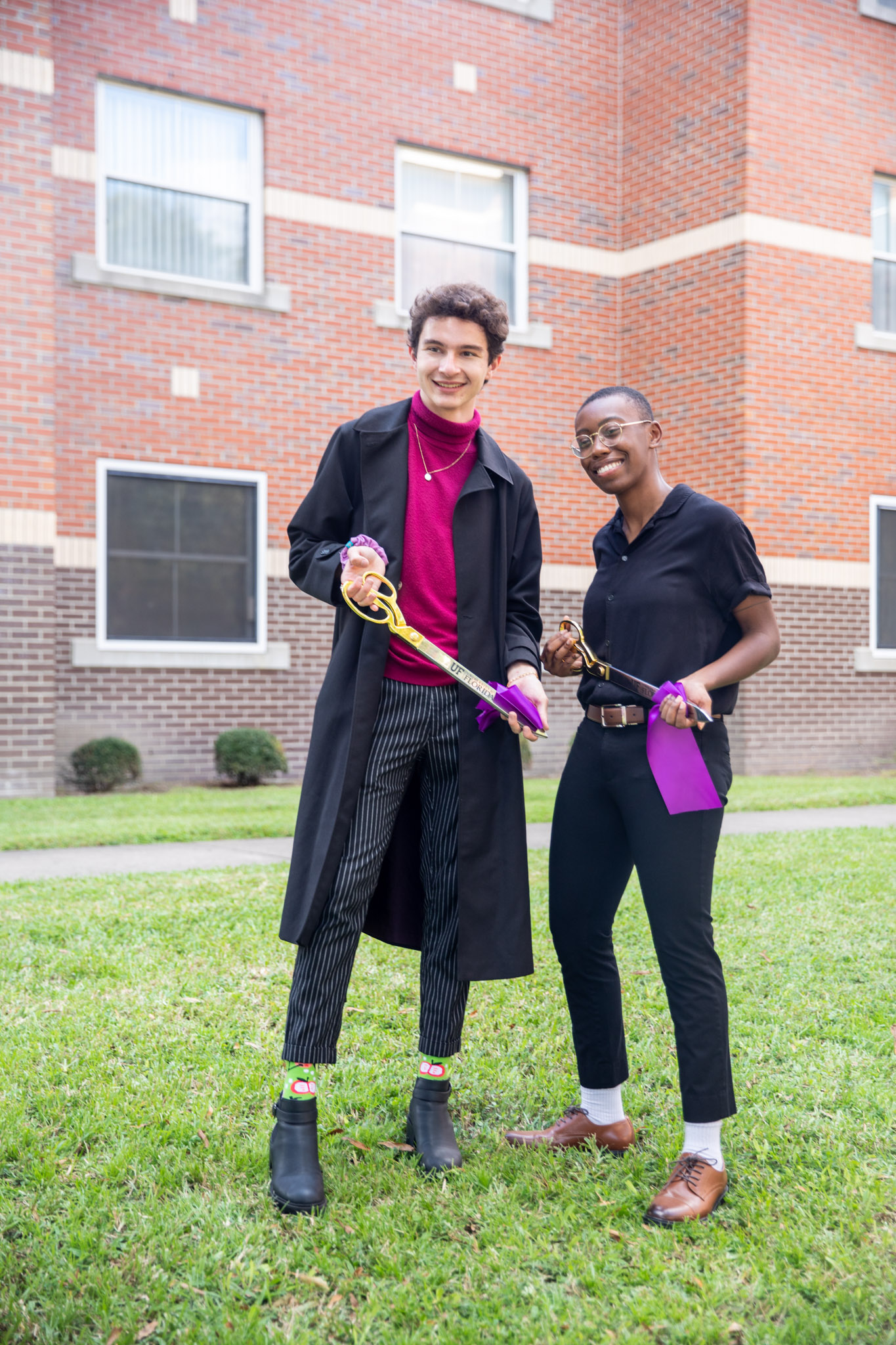 two students pose with ceremonial ribbon cutting scissors and purple ribbon.