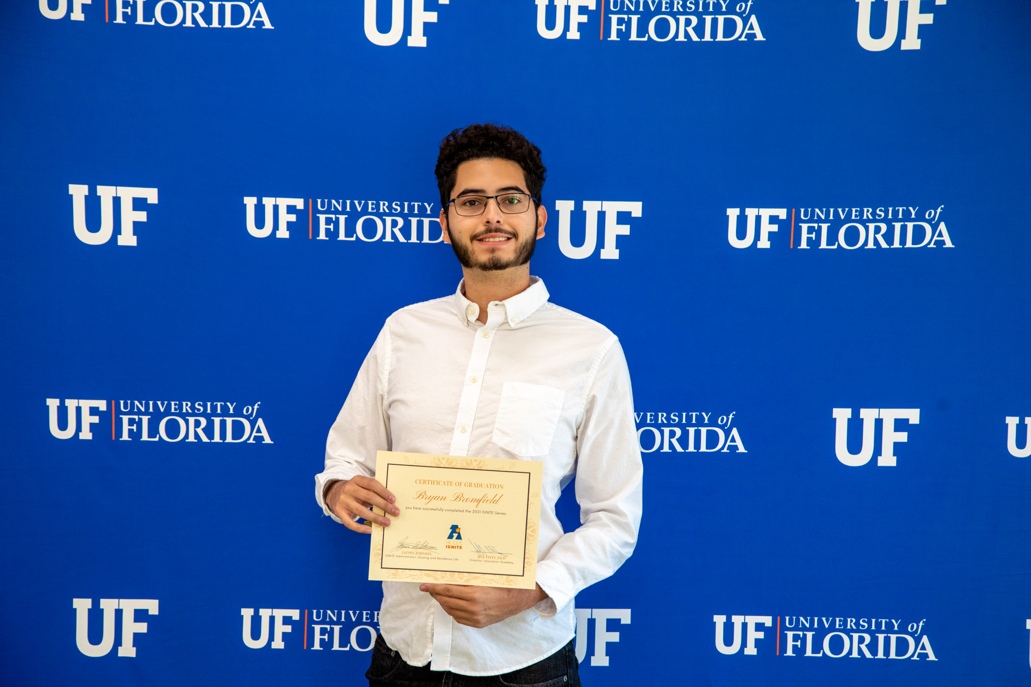 A student holds a certificate up in front of a UF step and repeat.