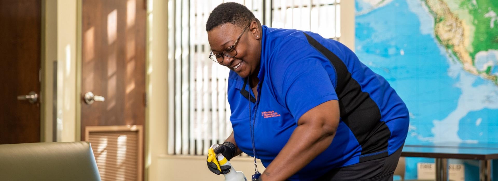 A custodial services staff member cleans furniture in a common area.