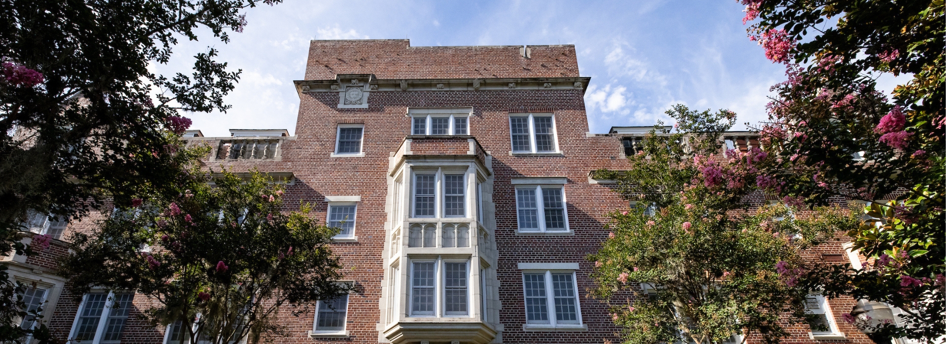The top of Murphree Hall stands on a sunny morning surrounded by green foliage.